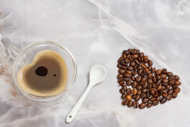 Glass cup of coffee, a spoon and roasted coffee beans on the kitchen table. Top view.