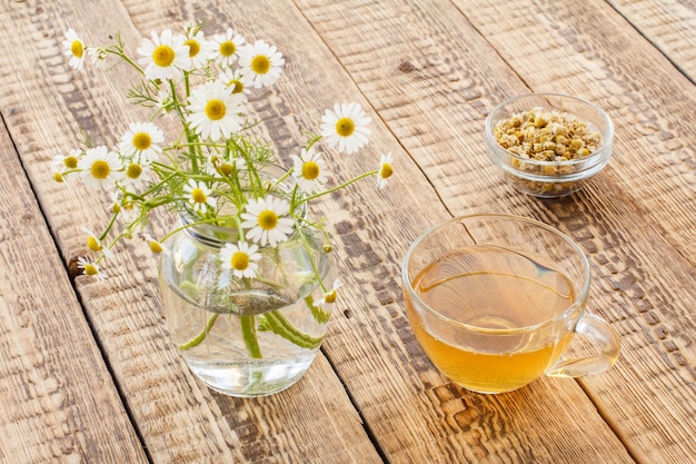 Glass cup of green tea, jar with white chamomile flowers and dry flowers of matricaria chamomilla