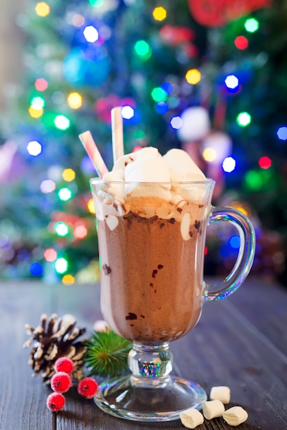 Glass cup of hot cocoa with mini marshmallows with pine boughs a rustic background