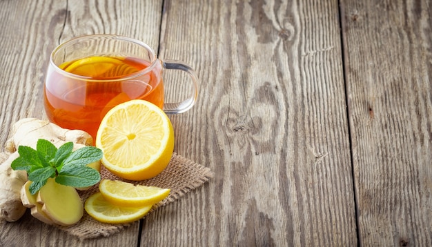 A glass cup of tea with lemon, mint and ginger on wooden rustic table.