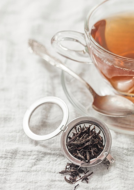 Glass cup with hot black tea and infuser with loose tea on white towel