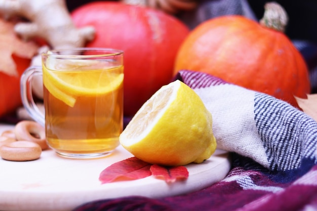 Glass cup with warm tea with lemon close-up on the background of pumpkins