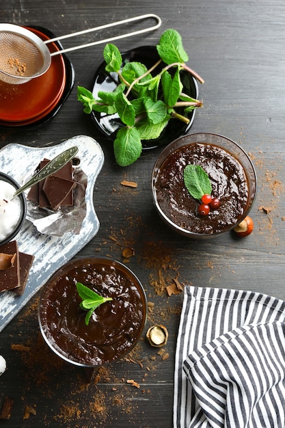 Glass cups of chocolate dessert with fresh mint on black wooden table