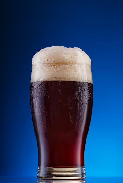 Glass of dark beer with foam on blue background