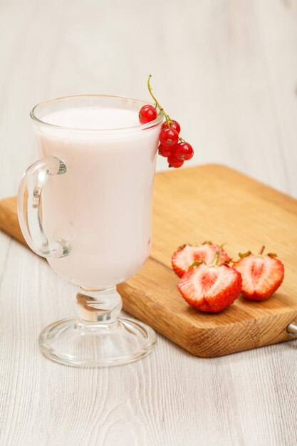 Glass of delicious strawberry yogurt with mint leaves and fresh strawberries on wooden cutting board