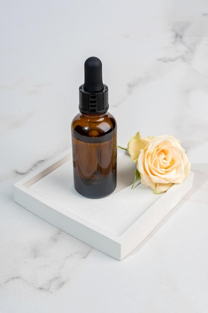 Glass dropper bottle with beauty oil or serum on ceramic tray on marble background Skincare products with beautiful daylight Trending concept natural cosmetic with rose essence Beauty concept