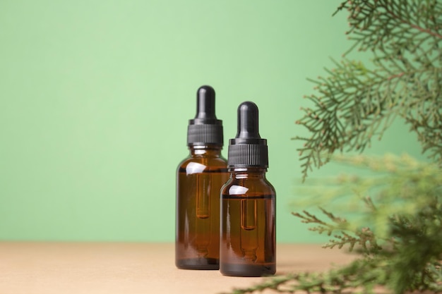 Glass dropper bottles with cosmetic oil essential or serum on green background with thuja branches Hyaluronic acid oil serum with collagen and peptides skin care product