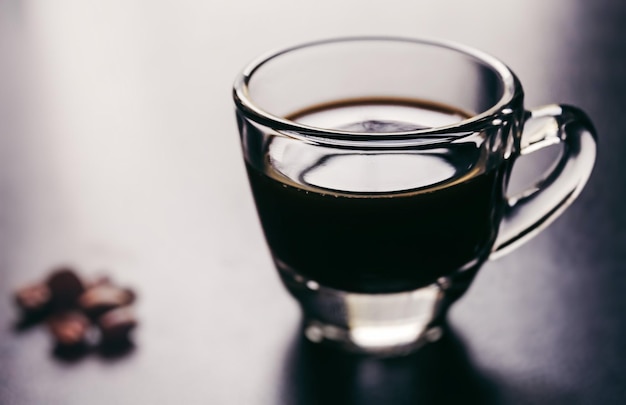 A glass of espresso coffee sits on a table next to a chocolate chip cookie.