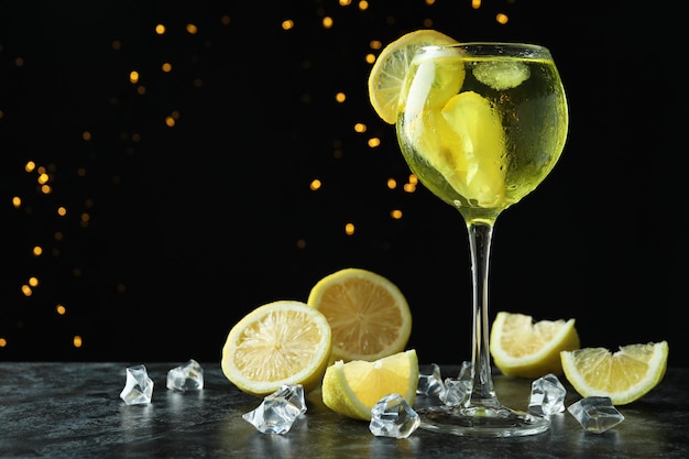 Glass of fresh citrus cocktail and ingredients against dark background with bokeh