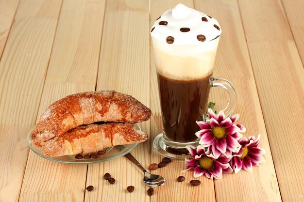 Glass of fresh coffee cocktail and saucer with bagels on wooden background