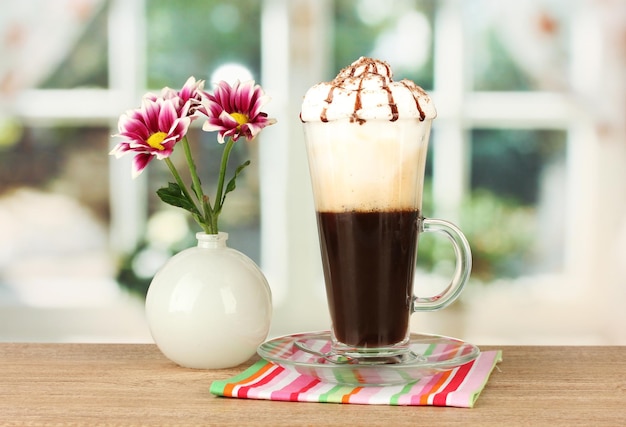 Glass of fresh coffee cocktail and vase with flower on wooden table closeup