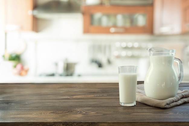 Glass of fresh milk and jug on wooden tabletop with blur kitchen as background.