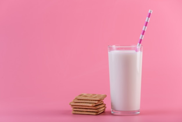 Glass of fresh milk with a straw and cookies on a pink background. Colorful minimalism. Healthy dairy products