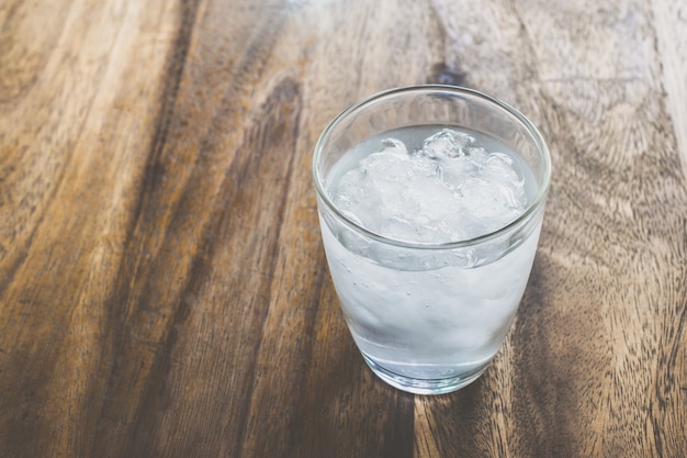 Glass of fresh mineral water with ice cubes on wood table with vintage color