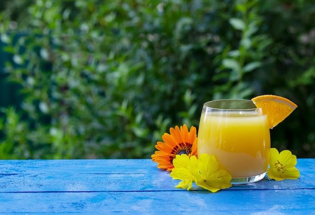 Glass of fresh orange juice garnished with a slice of ripe orange and flowers on the blue wooden table