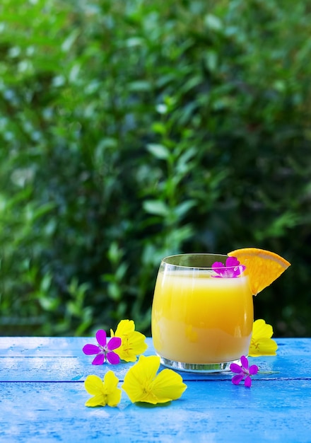 Glass of fresh orange juice garnished with a slice of ripe orange and flowers on the blue wooden table