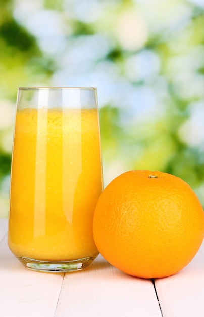 Glass of fresh orange juice on wooden table on green background