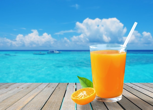 A glass of fresh orange juice on a wooden terrace by the sea in sunny day with copy space