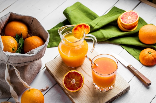 Glass of fresh pressed orange juice and blood oranges on wooden table. Bright summer mood. Top view