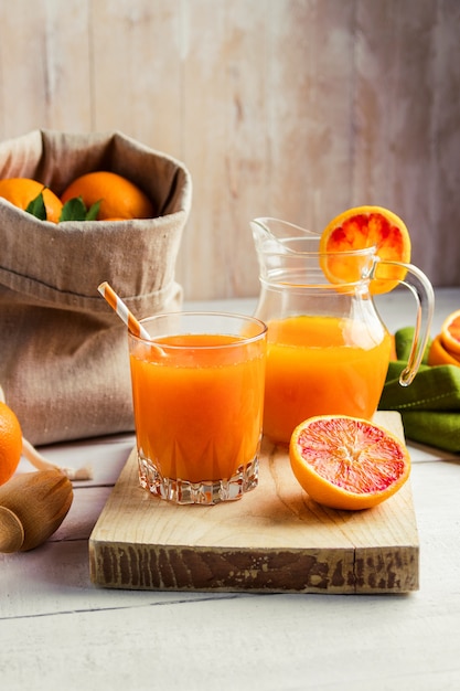 Glass of fresh pressed orange juice and blood oranges on wooden table.