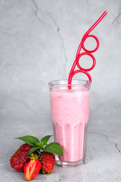 Glass of fresh strawberry milkshake smoothie and fresh strawberries on gray background Healthy food and drink concept