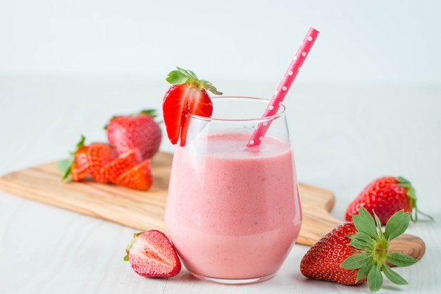 Glass of fresh strawberry milkshake, smoothie and fresh strawberries on pink, white and wooden background. Healthy food and drink concept.