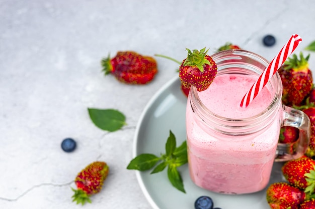 Glass of fresh strawberry milkshake or smoothie on gray background top view