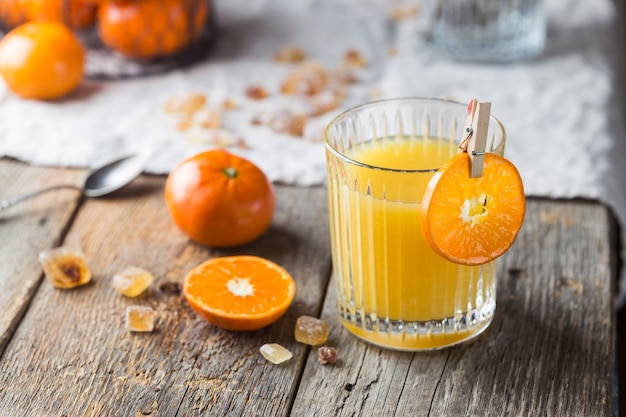 Glass of fresh tangerine juice with ripe tangerines on old wooden table, rustic style