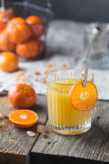 Glass of fresh tangerine juice with ripe tangerines on old wooden table, rustic style