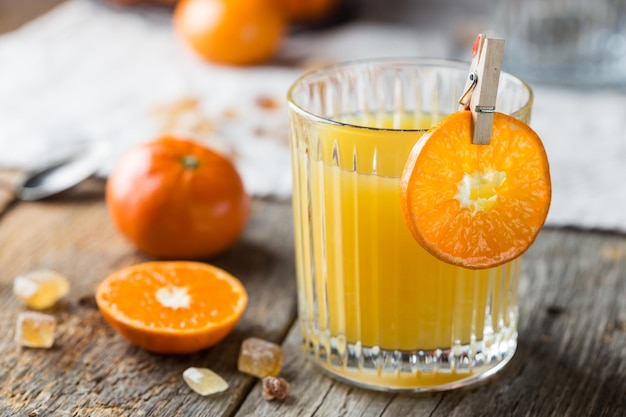 Glass of fresh tangerine juice with ripe tangerines on old wooden table, rustic style