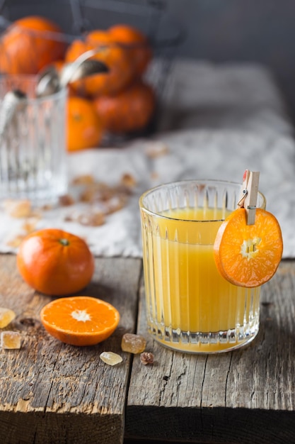 Glass of fresh tangerine juice with ripe tangerines on old wooden table, rustic style