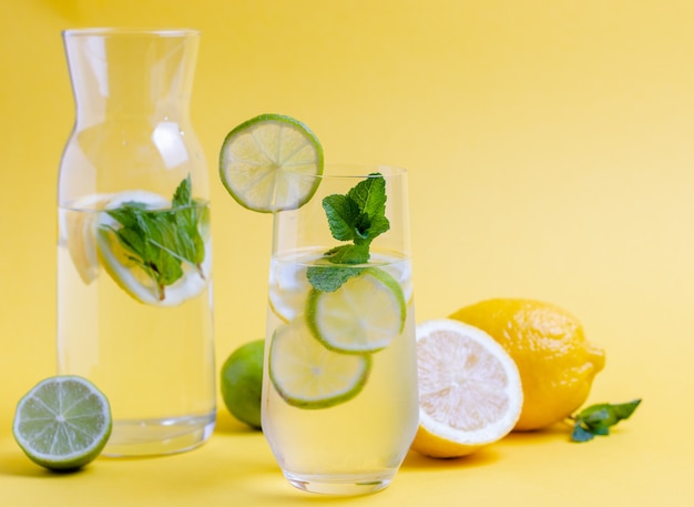 Glass of fresh water with lime slices and mint leave on yellow background