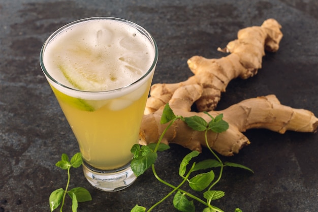 A glass of ginger beer on a black marble background with ginger and fresh mint. Ginger beer is a thirst-quenching and low alcoholic drink.