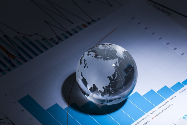 Glass globe ball in light rays on background of business charts