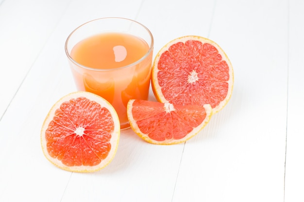 A glass of grapefruit juice and fresh grapefruit on a white wooden table close-up.