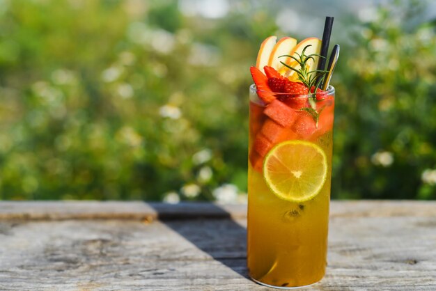 Glass of green tropical tea with lime, orange, watermelon and apple against green summer background