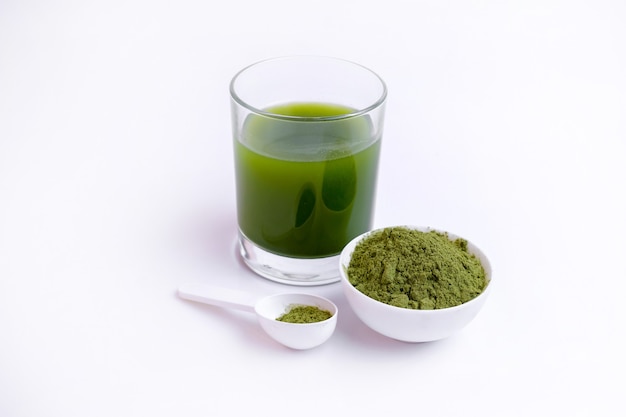 Glass of green vegetable juice  and Powder of vegetables on spoon at white surface