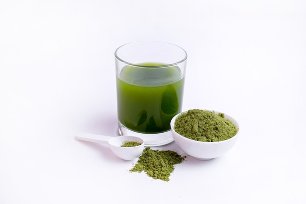 Glass of green vegetable juice  and Powder of vegetables on spoon at white surface