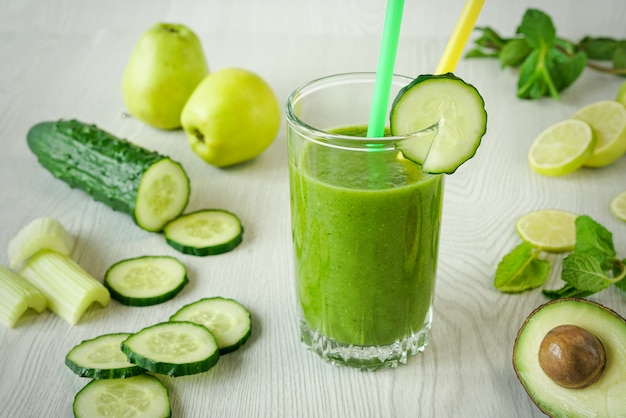 A glass of green vegetable smoothies on a white wooden background