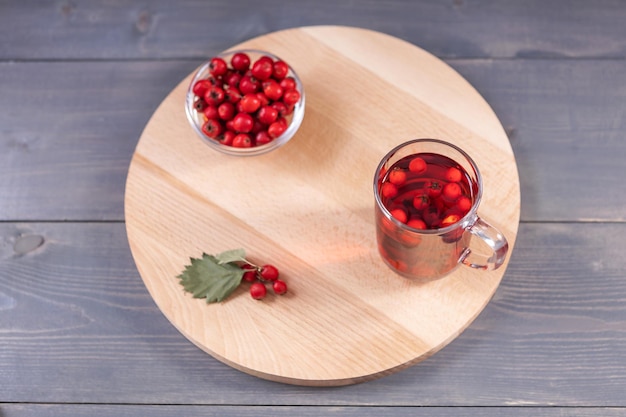 Glass of hawthorn juice and fresh hawthorn berries on a wooden board