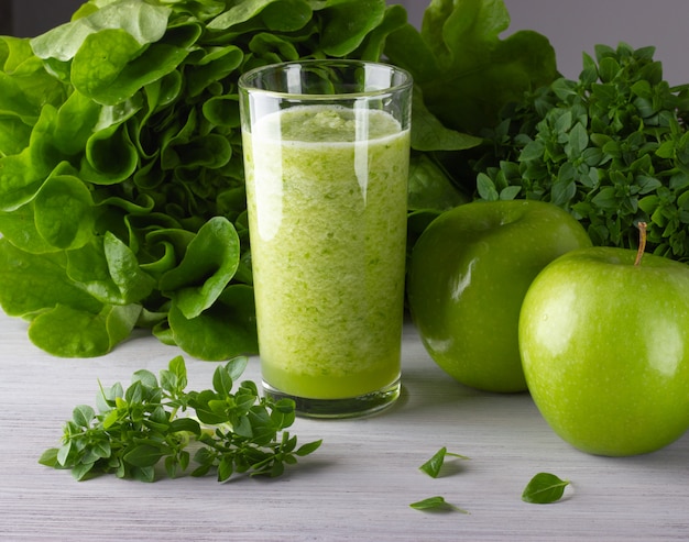 A glass of healthy green smoothie with apple and leaves on the white wooden table