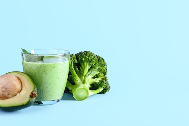 Glass of healthy smoothie with avocado and broccoli on color surface