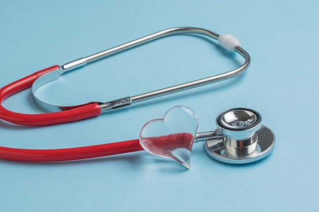 A glass heart and a red stethoscope on a blue background. The concept of treatment of various diseases.