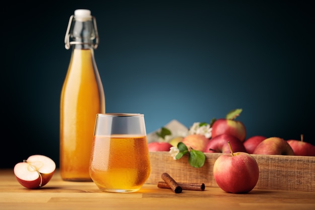 Glass of homemade apple cider or juice, red fresh apples from the garden and a bottle on background