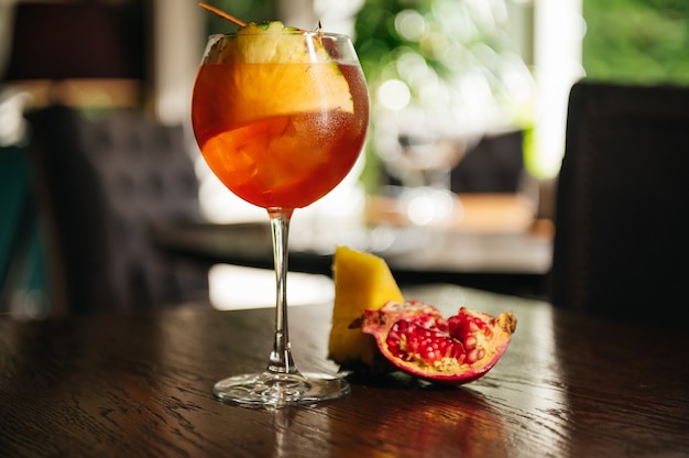 Glass of ice cold Aperol spritz cocktail served in a wine glass with pineapple and garnet, placed on a table in restaurant