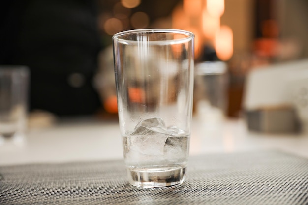 A glass of ice sits on a table with a fireplace in the background.