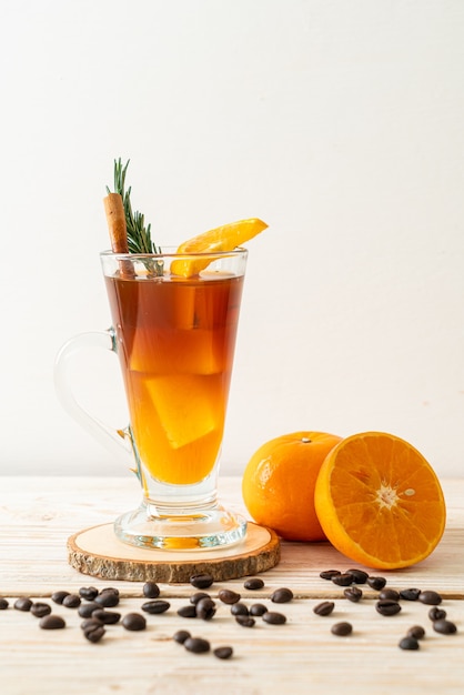 A glass of iced americano black coffee and layer of orange and lemon juice decorated with rosemary and cinnamon