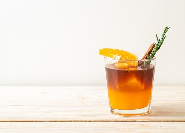 A glass of iced americano black coffee and layer of orange and lemon juice decorated with rosemary and cinnamon