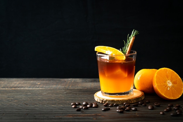 A glass of iced americano black coffee and layer of orange and lemon juice decorated with rosemary and cinnamon