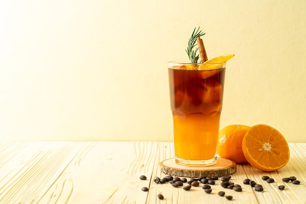 A glass of iced americano black coffee and layer of orange and lemon juice decorated with rosemary and cinnamon